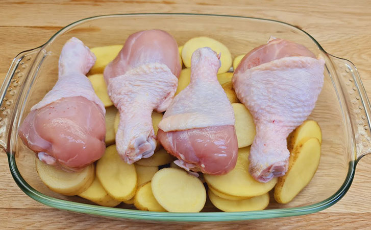 Кладем куриные голени поверх картошки и закрываем фольгой: гарнир и горячее готовы за 50 минут