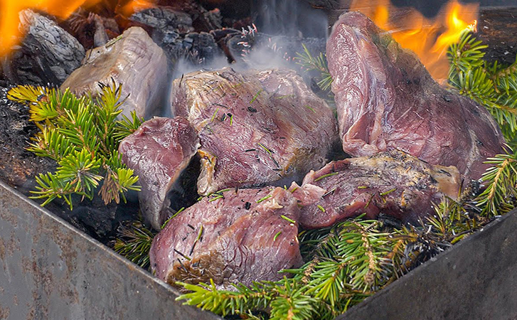 Кладем мясо прямо в угли и накрываем еловыми ветками. Обходимся без шампуров и решеток